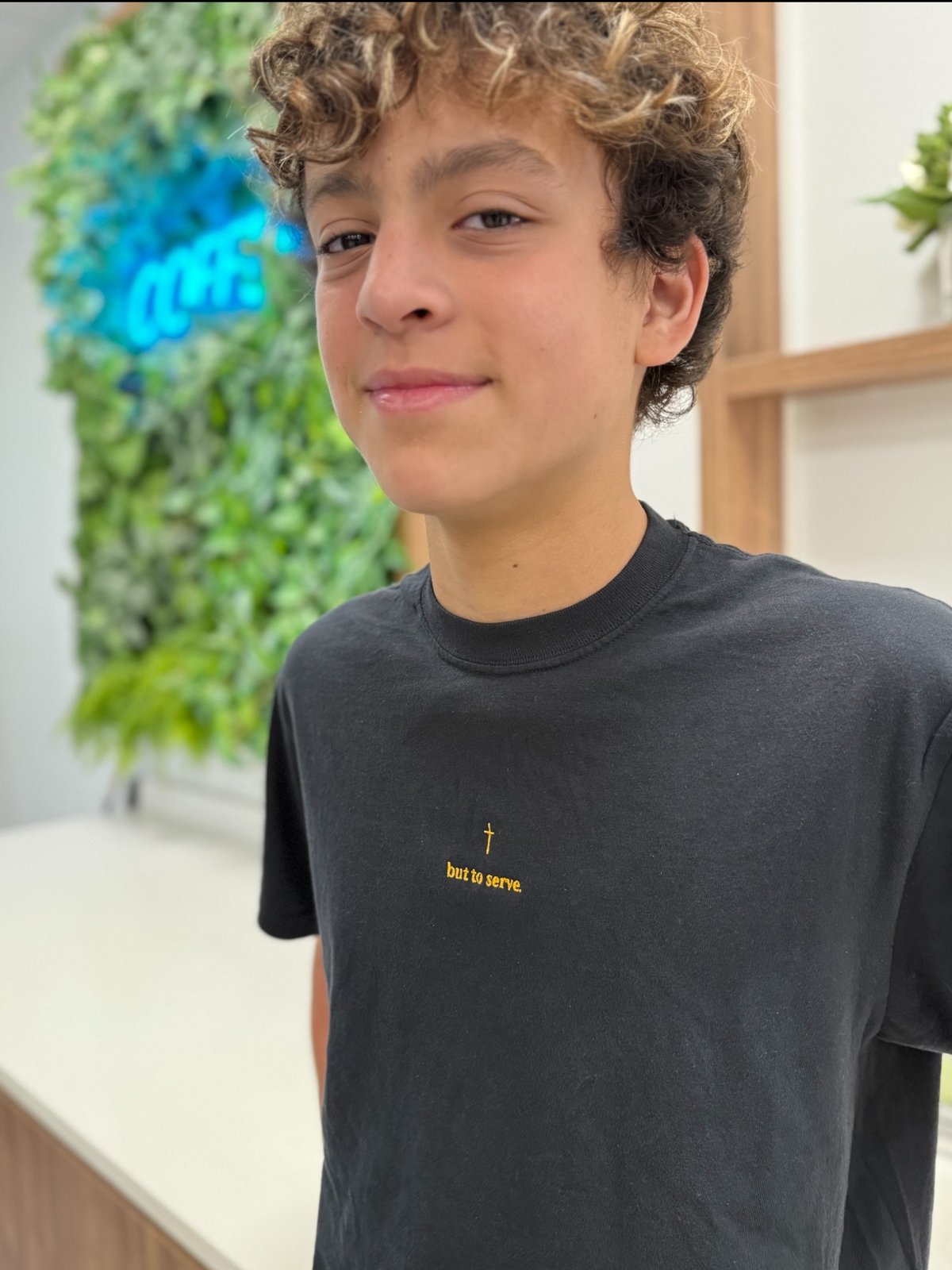 JD Valletta wearing the black But to Serve tee with gold embroidery